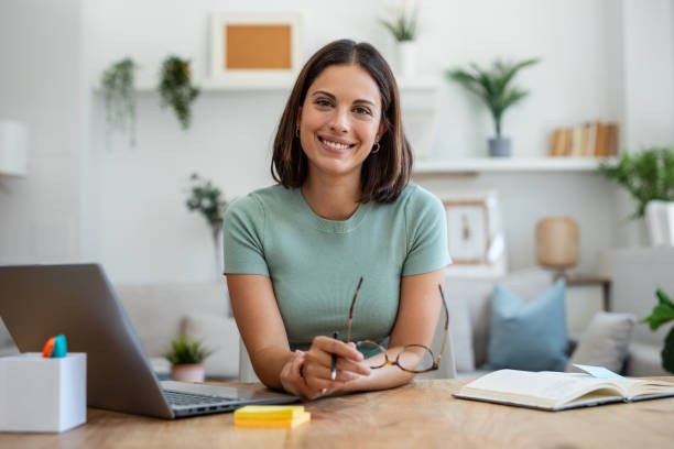 Shot of beautiful business woman working with laptop while looking at camera in living room at home.